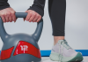 Donna che solleva un kettlebell da 12 kg durante un allenamento fitness indoor con abbigliamento sportivo e scarpe da training