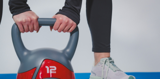 Donna che solleva un kettlebell da 12 kg durante un allenamento fitness indoor con abbigliamento sportivo e scarpe da training