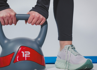 Donna che solleva un kettlebell da 12 kg durante un allenamento fitness indoor con abbigliamento sportivo e scarpe da training